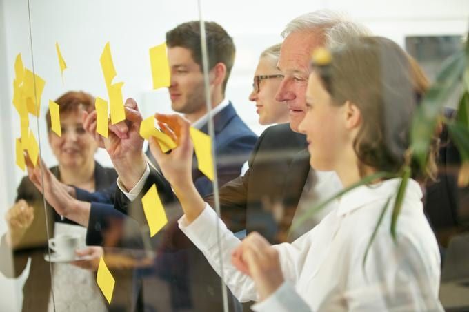 Personnes en tenue de bureau qui collent des post-it jaunes sur une paroi vitrée