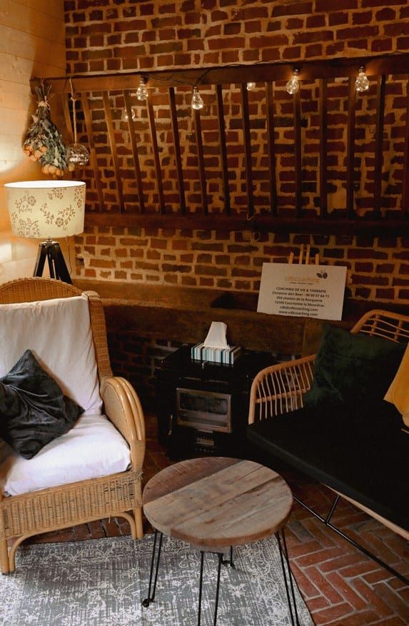 Le cabinet à Courtonne-la-Meurdrac, près de Lisieux : fauteuils en rotin, mur de briques, guirlande lumineuse et panneau CDB Coaching