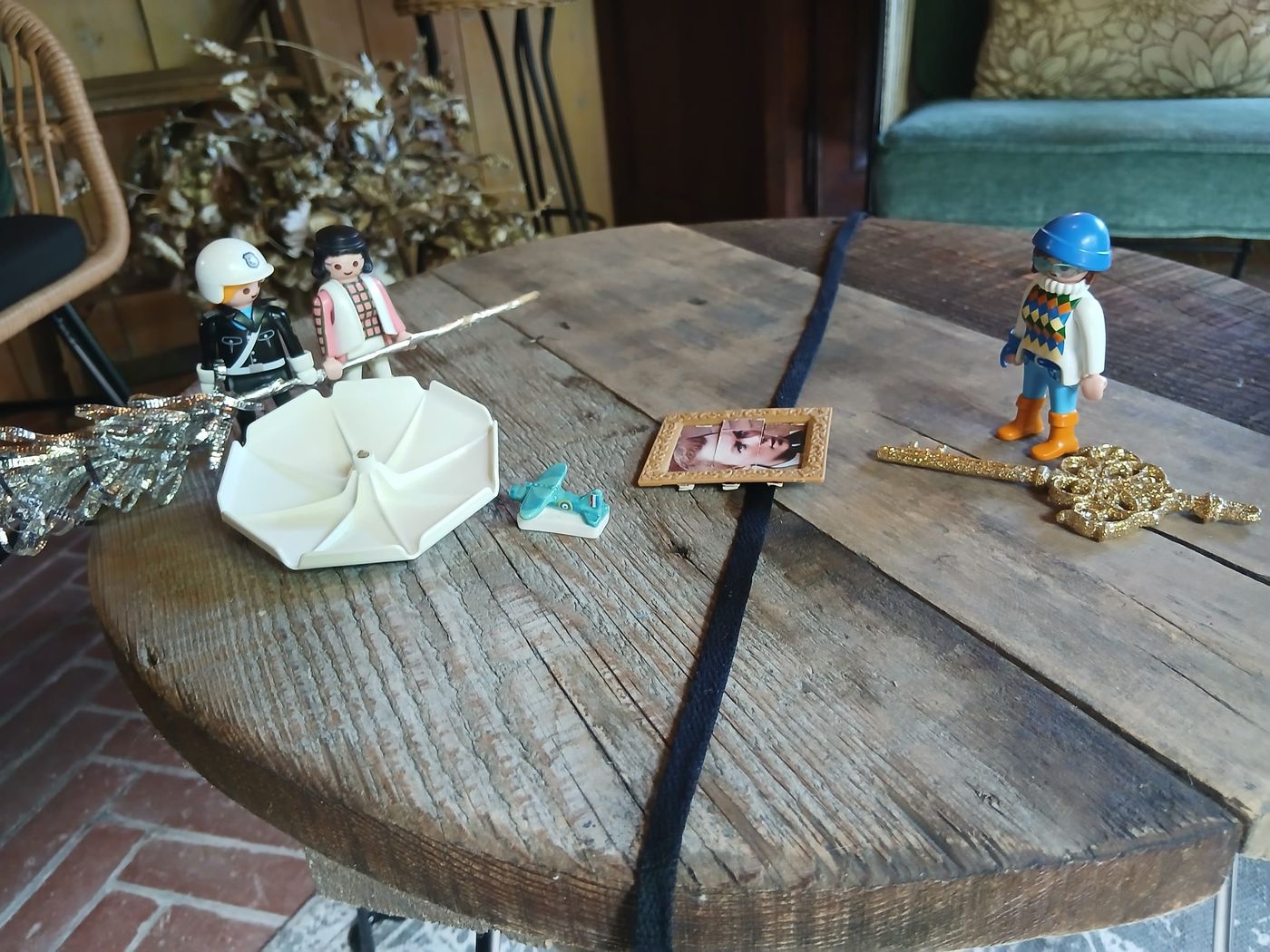 Petites figurines (policier, femme, enfant) et objets posés sur une table ronde en bois partagée par un cordon noir
