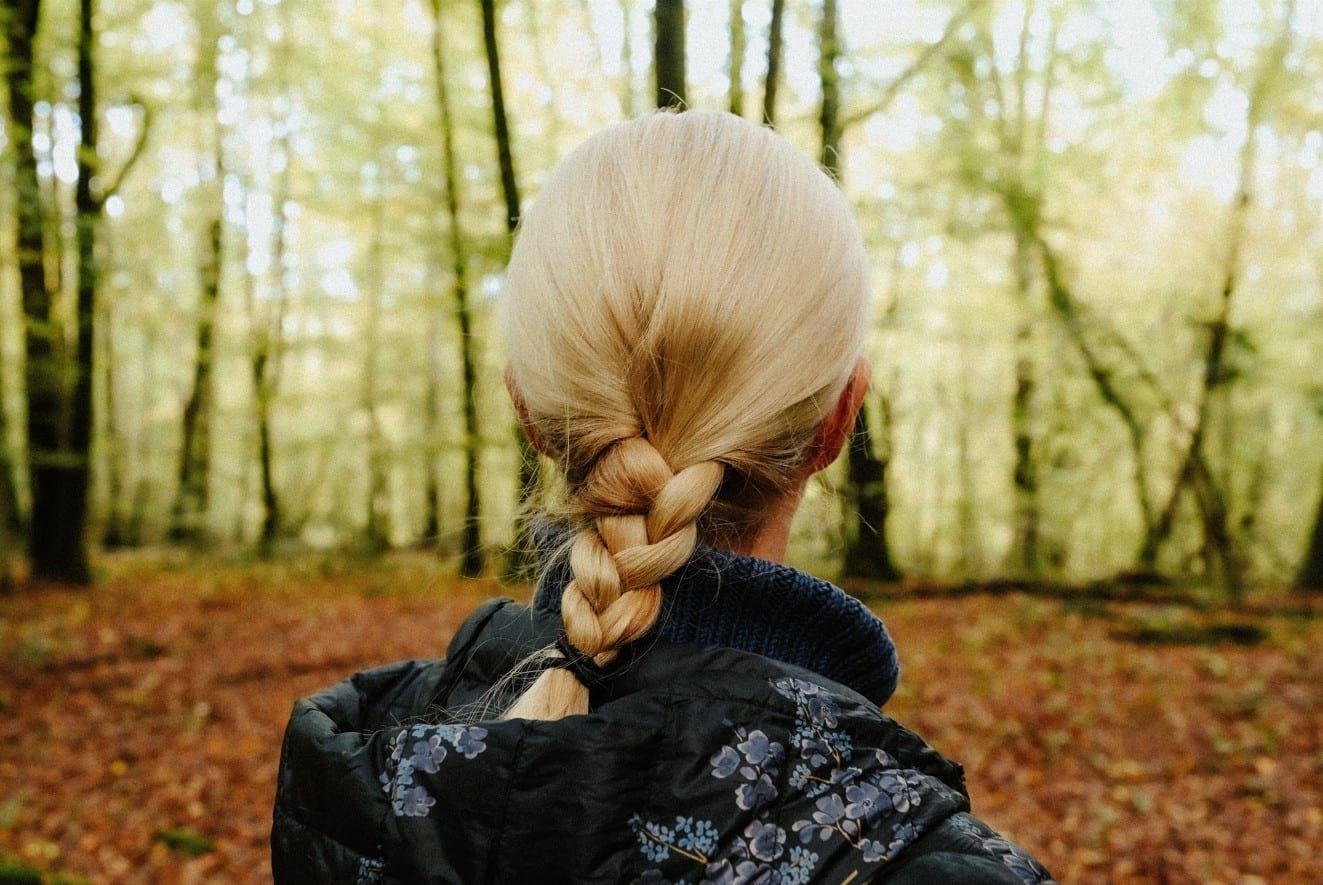 Femme de dos aux cheveux blonds tressés, dans une forêt de hêtres aux feuilles d'automne