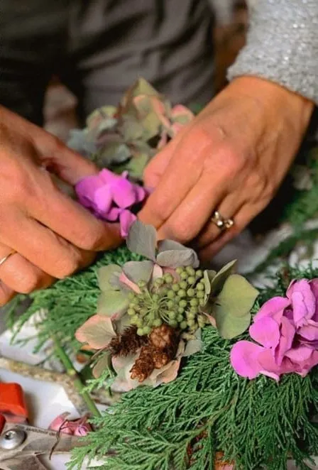 Mains composant une couronne d’hortensias et de thuya