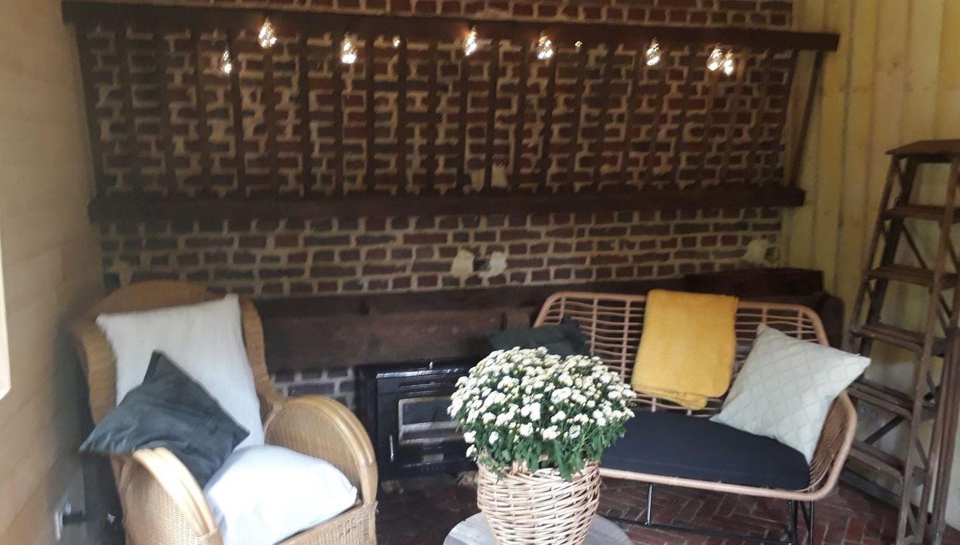 Coin salon du cabinet à Courtonne-la-Meurdrac, près de Lisieux : fauteuil en rotin, plaid jaune et poêle à bois